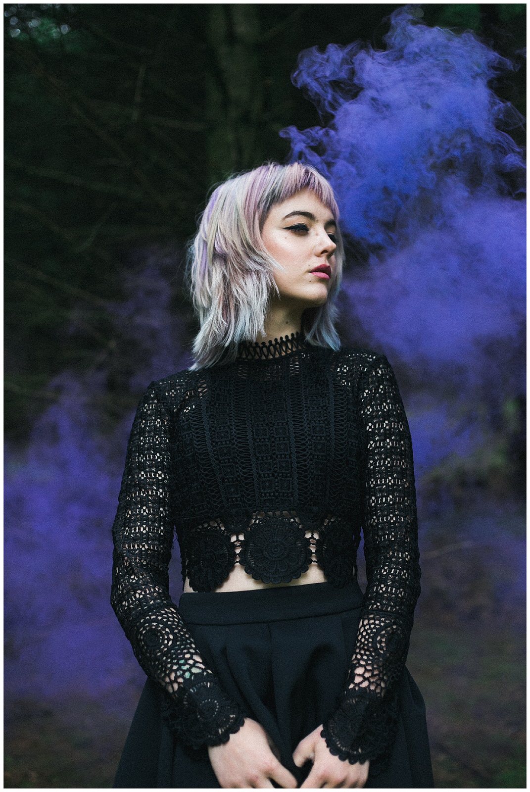 Portrait of a bride in a black wedding outfit in front of a purple smoke bomb 