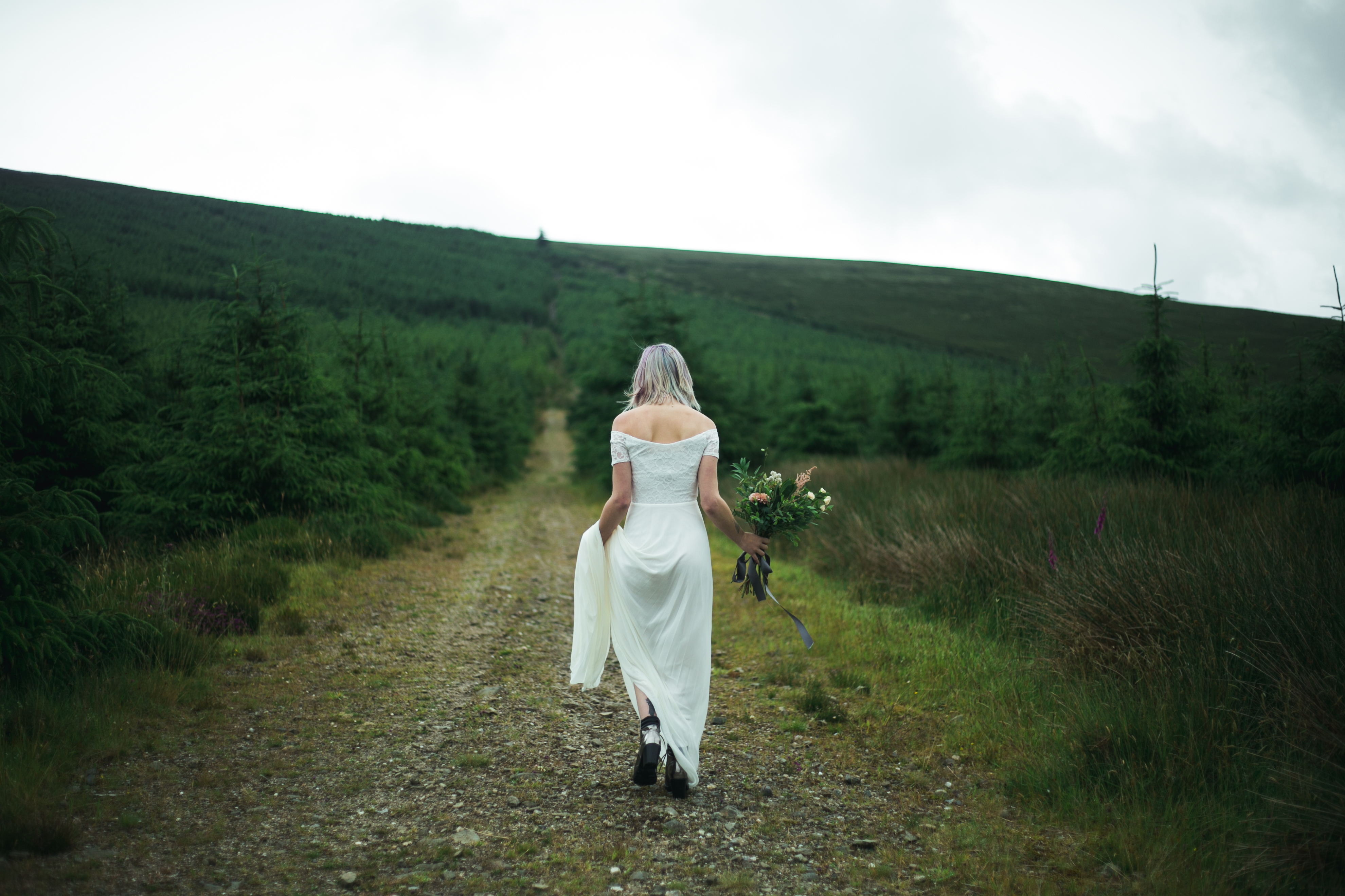 Bride holding up the hem of her floor length wedding dress as she walks through the countryside
