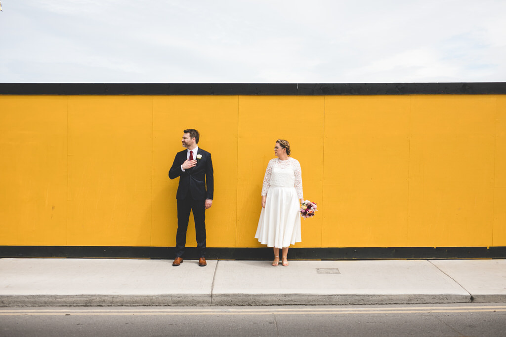 Funky colourful wedding photo in front of bright yellow hoarding 